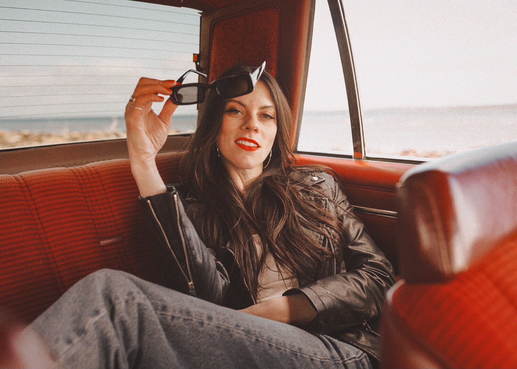 Elyse Aeryn seated in the back of a vintage car by the coast
