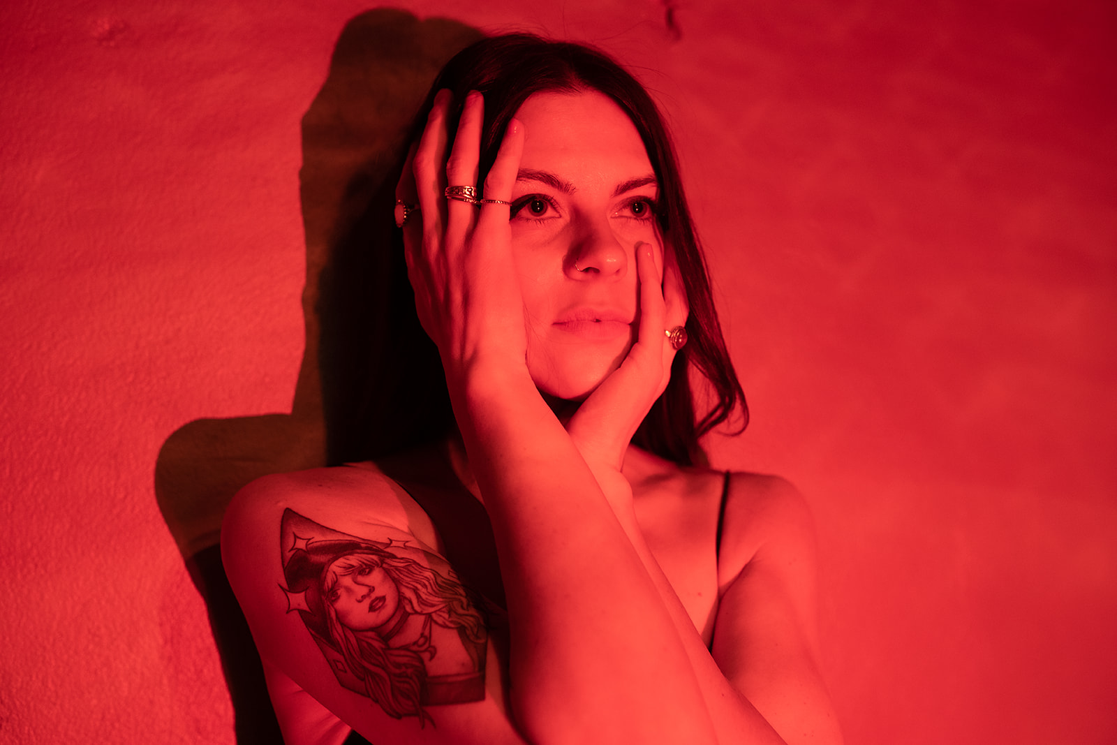 Elyse Aeryn bathed in red light with her eyes closed and hands held to her face