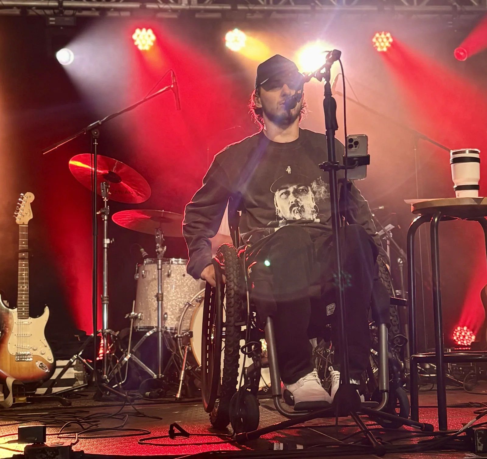 Connor Hirtle singing into a microphone with HIRTLE under red stage lights